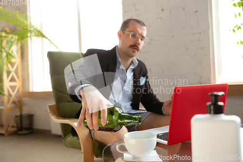 Image of Young man without pants but in jacket working on a computer, laptop. Remote office during coronavirus, fun and comfortable work in underpants