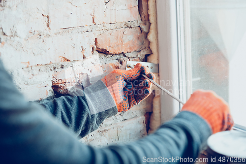 Image of Close up of hands of repairman, professional builder working indoors, installs window