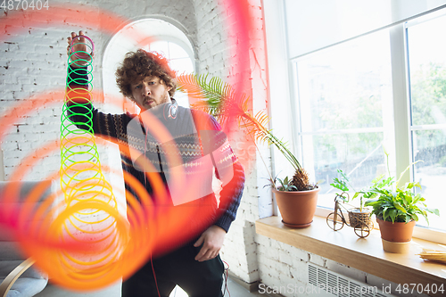 Image of Portrait of millenial boy using retro toys, meeting things from the past and having fun, nostalgic, using rainbow spring toy