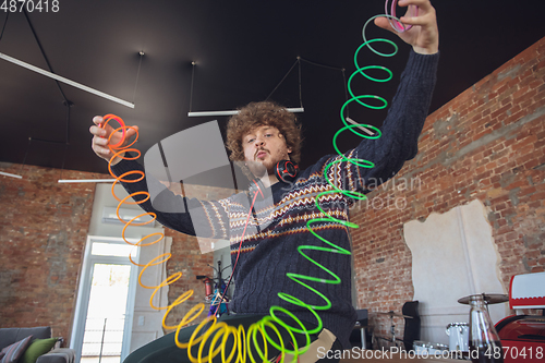 Image of Portrait of millenial boy using retro toys, meeting things from the past and having fun, nostalgic, using rainbow spring toy