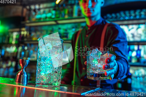 Image of Close up of barman finishes preparation of alcoholic cocktail in multicolored neon light