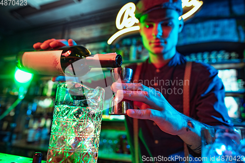 Image of Barman finishes preparation of alcoholic cocktail with shot in multicolored neon light