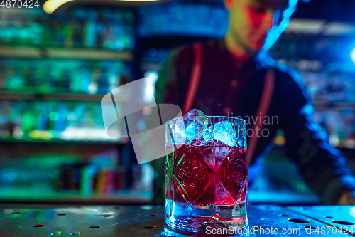 Image of Close up of barman finishes preparation of alcoholic cocktail in multicolored neon light