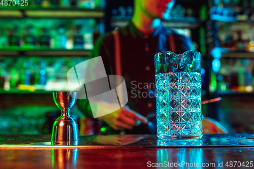 Image of Close up of barman finishes preparation of alcoholic cocktail in multicolored neon light