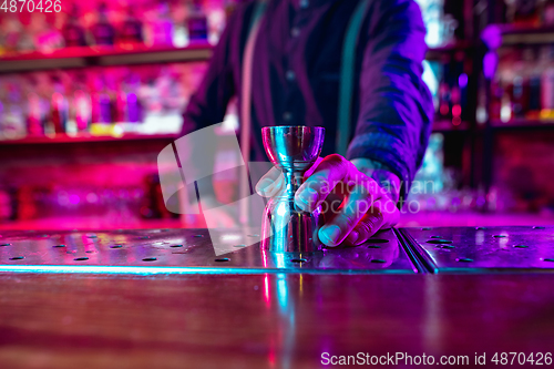 Image of Close up of barman finishes preparation of alcoholic shot in multicolored neon light