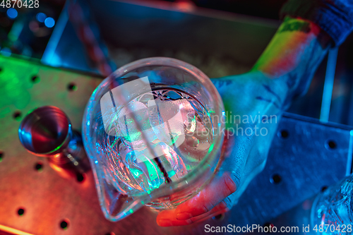Image of Top view of barman finishes preparation of alcoholic liquor and ice cocktail in multicolored neon light