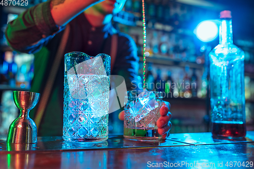 Image of Close up of barman finishes preparation of alcoholic liquor and ice cocktail in multicolored neon light