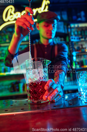 Image of Close up of barman finishes preparation of alcoholic cocktail in multicolored neon light