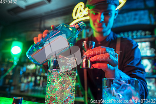 Image of Barman finishes preparation of alcoholic cocktail with shot in multicolored neon light