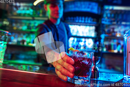 Image of Close up of barman finishes preparation of alcoholic cocktail in multicolored neon light