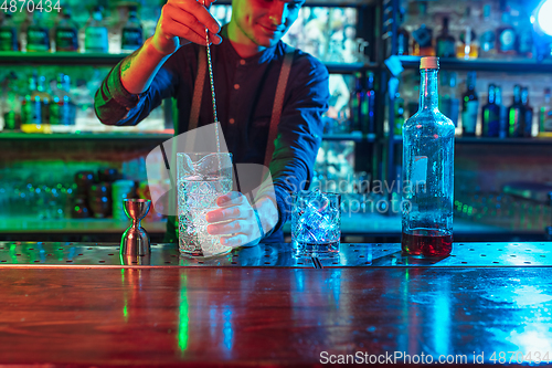 Image of Close up of barman finishes preparation of alcoholic liquor and ice cocktail in multicolored neon light