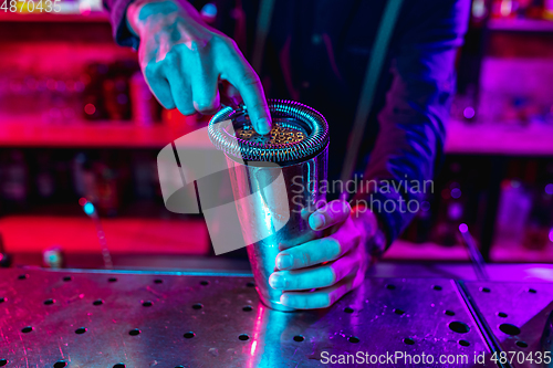 Image of Close up of barman finishes preparation of alcoholic cocktail with shaker in multicolored neon light