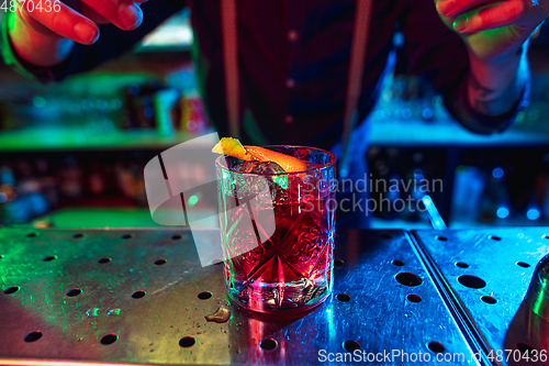 Image of Close up of barman finishes preparation of alcoholic cocktail in multicolored neon light