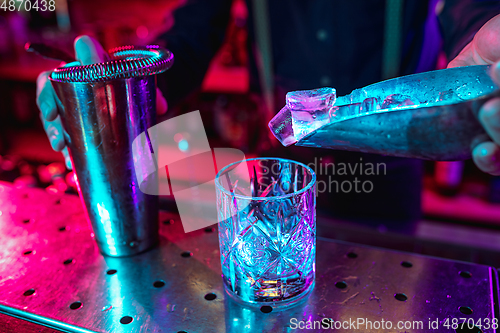 Image of Close up of barman finishes preparation of alcoholic cocktail with shaker in multicolored neon light