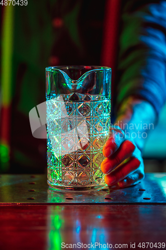 Image of Close up of barman finishes preparation of alcoholic cocktail in multicolored neon light