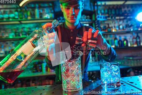 Image of Barman finishes preparation of alcoholic cocktail with shot in multicolored neon light