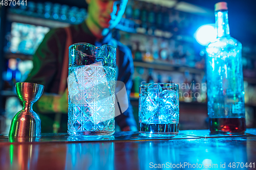 Image of Close up of barman finishes preparation of alcoholic cocktail in multicolored neon light