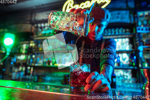 Image of Close up of barman finishes preparation of alcoholic cocktail in multicolored neon light
