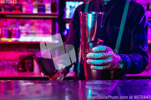 Image of Close up of barman finishes preparation of alcoholic cocktail with shaker in multicolored neon light