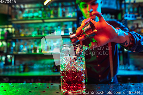 Image of Barman finishes preparation of alcoholic cocktail with shot in multicolored neon light