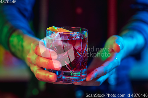 Image of Close up of barman finishes preparation of alcoholic cocktail in multicolored neon light