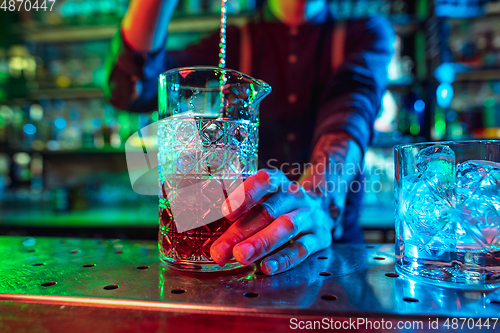 Image of Close up of barman finishes preparation of alcoholic cocktail in multicolored neon light