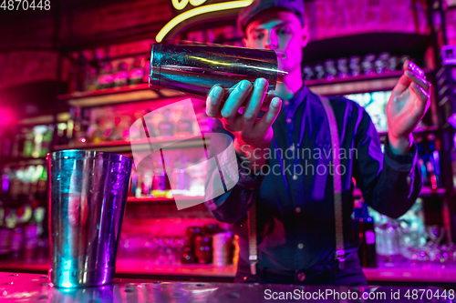 Image of Barman finishes preparation of alcoholic cocktail with shaker in multicolored neon light