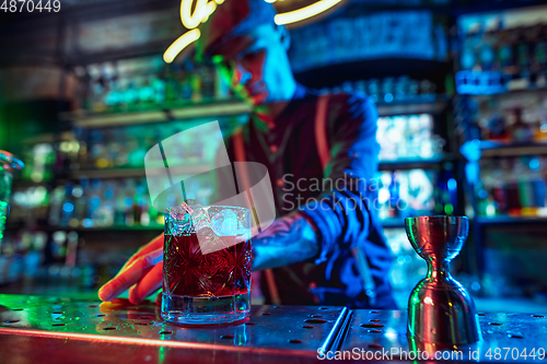 Image of Close up of barman finishes preparation of alcoholic cocktail in multicolored neon light