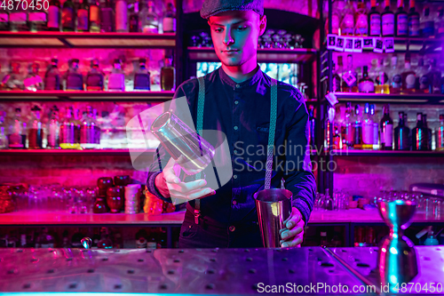 Image of Barman finishes preparation of alcoholic cocktail with shaker in multicolored neon light