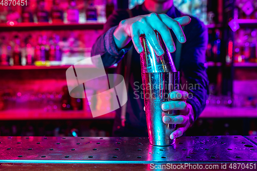 Image of Close up of barman finishes preparation of alcoholic cocktail with shaker in multicolored neon light