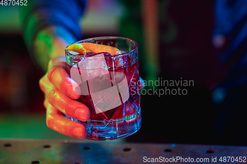 Image of Close up of barman finishes preparation of alcoholic cocktail in multicolored neon light