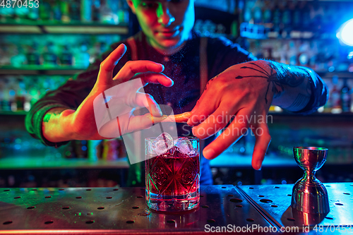 Image of Close up of barman finishes preparation of alcoholic cocktail in multicolored neon light