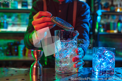 Image of Close up of barman finishes preparation of alcoholic cocktail in multicolored neon light