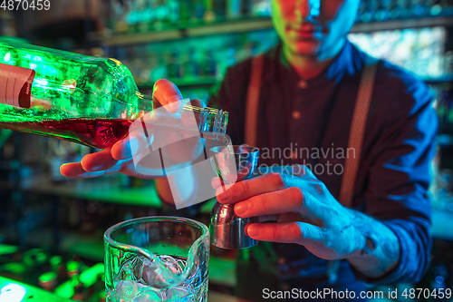 Image of Barman finishes preparation of alcoholic cocktail with shot in multicolored neon light