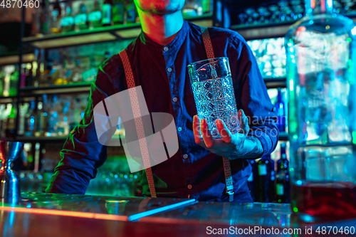 Image of Close up of barman finishes preparation of alcoholic cocktail in multicolored neon light