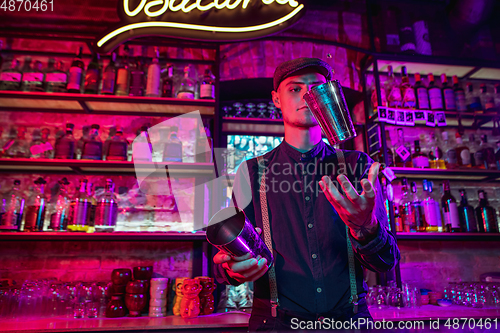 Image of Barman finishes preparation of alcoholic cocktail with shaker in multicolored neon light