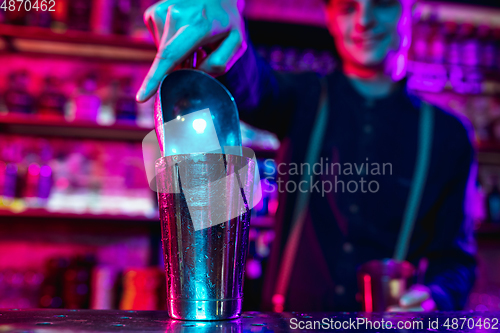Image of Close up of barman finishes preparation of alcoholic cocktail with shaker in multicolored neon light