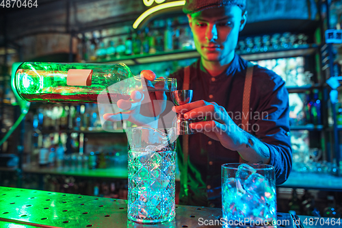 Image of Barman finishes preparation of alcoholic cocktail with shot in multicolored neon light