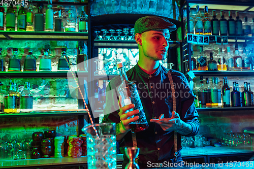 Image of Barman proposing alcoholic cocktails, shots, beverages to guest in multicolored neon light