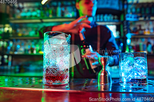 Image of Close up of barman finishes preparation of alcoholic cocktail with shot in multicolored neon light