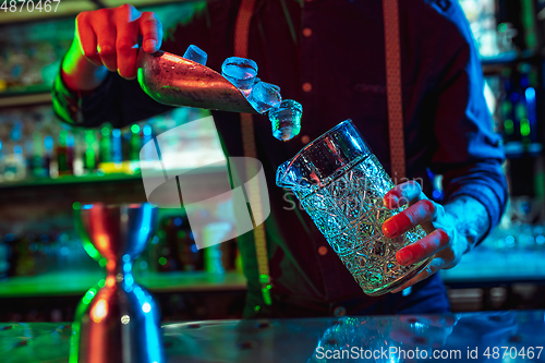 Image of Close up of barman finishes preparation of alcoholic cocktail in multicolored neon light