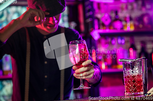 Image of Barman proposing alcoholic cocktails, shots, beverages to guest in multicolored neon light