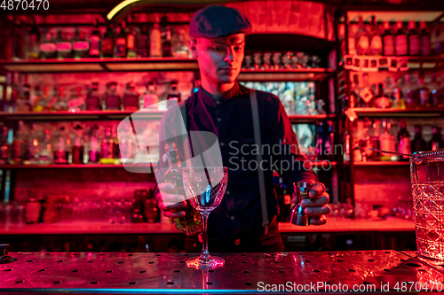 Image of Barman preparing the alcoholic cocktail in multicolored neon light, focus on glass