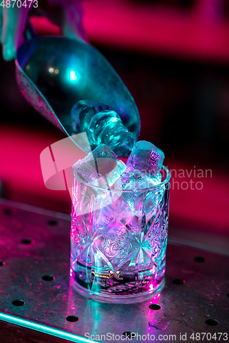 Image of Close up of alcoholic cocktail, beverage, drink, glass full of ice in multicolored neon light