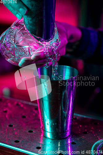 Image of Close up of barman finishes preparation of alcoholic cocktail, pouring drink in multicolored neon light