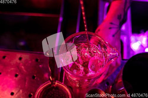 Image of Close up of barman finishes preparation of alcoholic cocktail, shaking ice in multicolored neon light