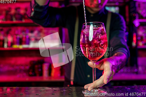 Image of Close up of barman finishes preparation of alcoholic cocktail, shaking drink in multicolored neon light, focus on glass