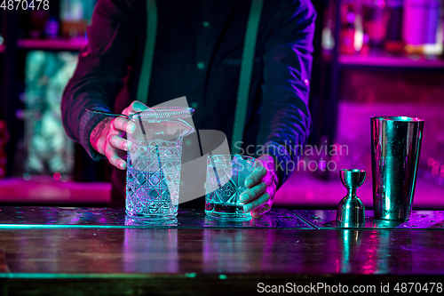 Image of Close up of barman finishes preparation of alcoholic cocktail in multicolored neon light