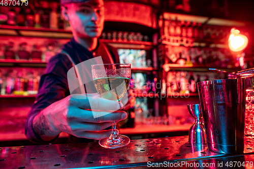 Image of Barman proposing alcoholic cocktails, shots, beverages to guest in multicolored neon light