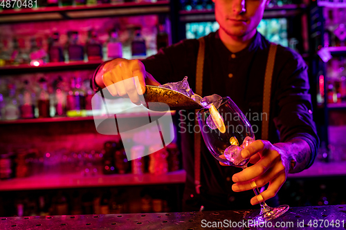 Image of Close up of barman finishes preparation of alcoholic cocktail, pouring drink in multicolored neon light